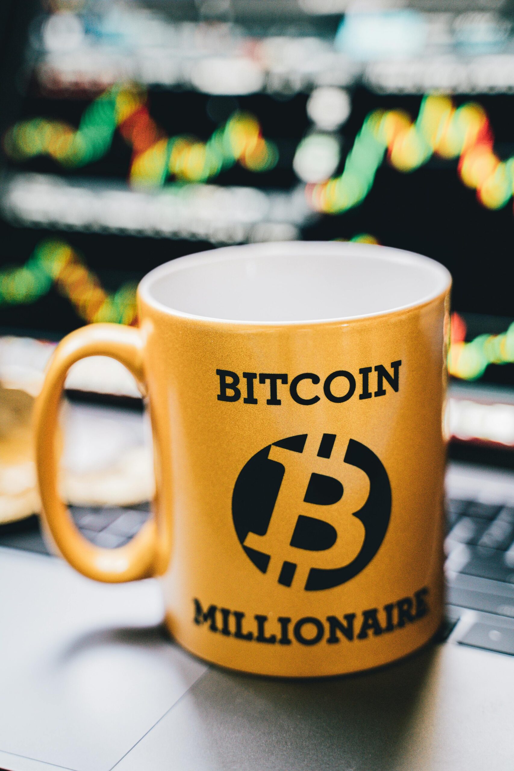 Close-up of a 'Bitcoin Millionaire' mug in front of a vibrant stock chart background.